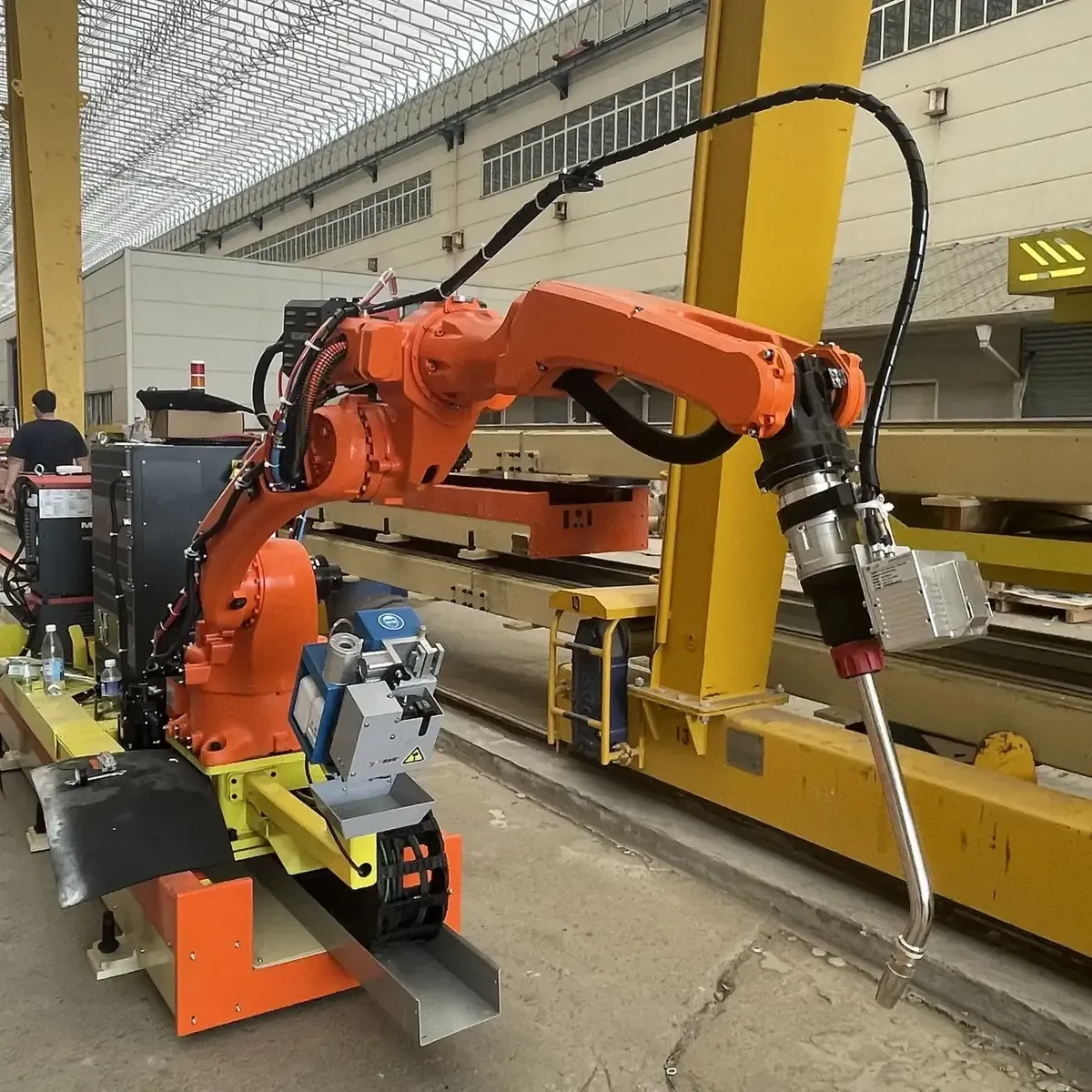 Orange welding robot with torch and vision sensor on a rail carriage.